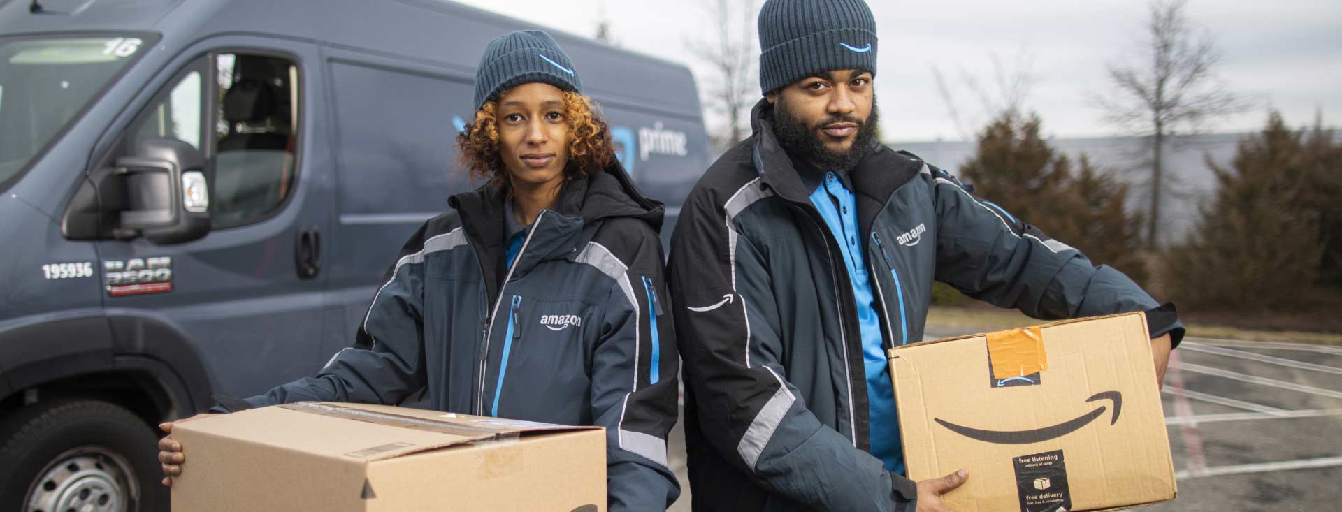 Amazon delivery person in uniform holding Amazon cardboard shipping box in front of open delivery van